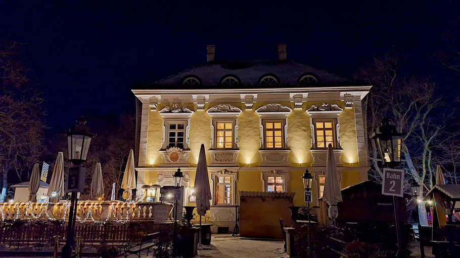 Historisches Gebäude leuchtet nachts, umgeben von Bäumen und Laternen.