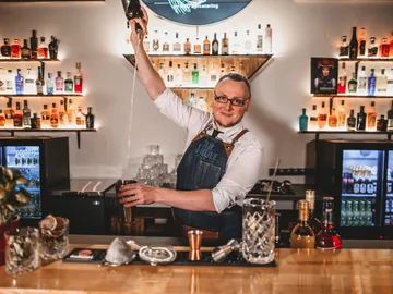 Bartender shakes cocktails behind a well-stocked bar.