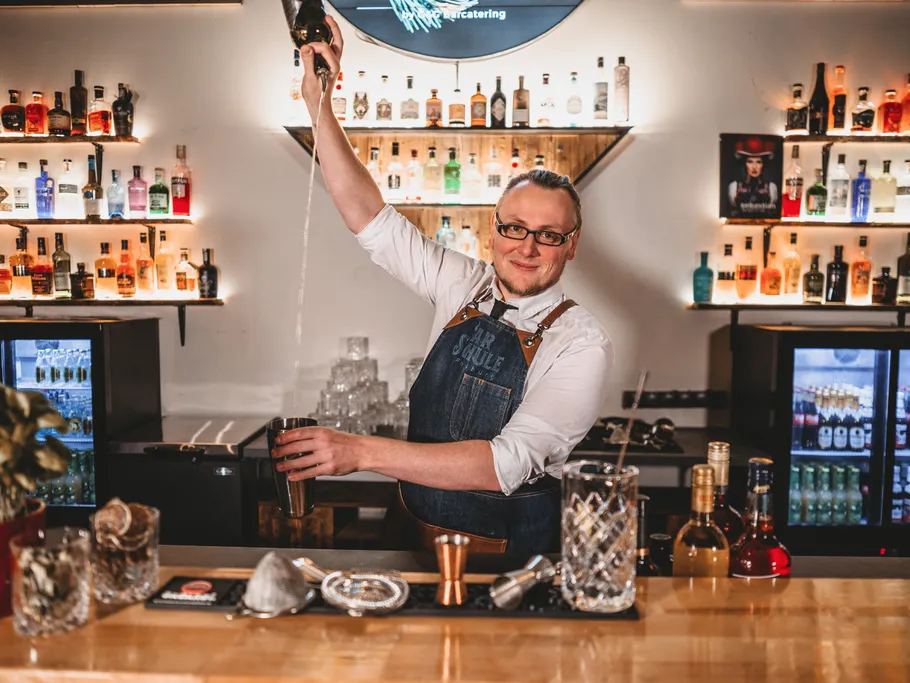 Bartender schüttelt Cocktails hinter einer gut gefüllten Bar.