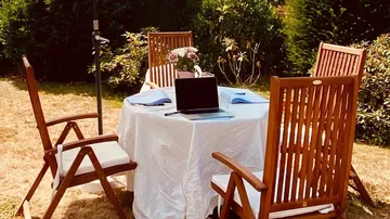 Holztisch mit Laptop und Stühlen im Garten.