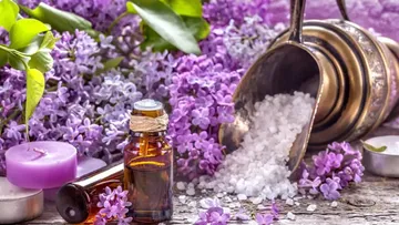 Flasche mit ätherischem Öl, umgeben von lilafarbenen Blumen.