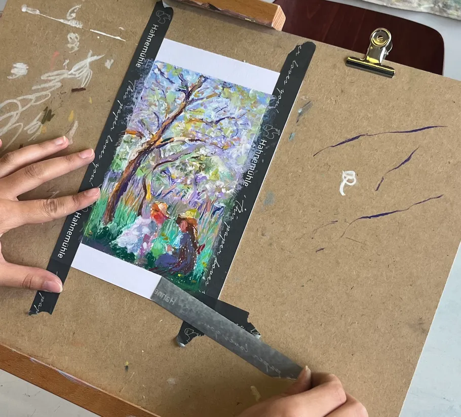 Two hands cut a piece of art on a table.