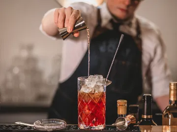 Bartender pouring liquor into iced mixing glass.