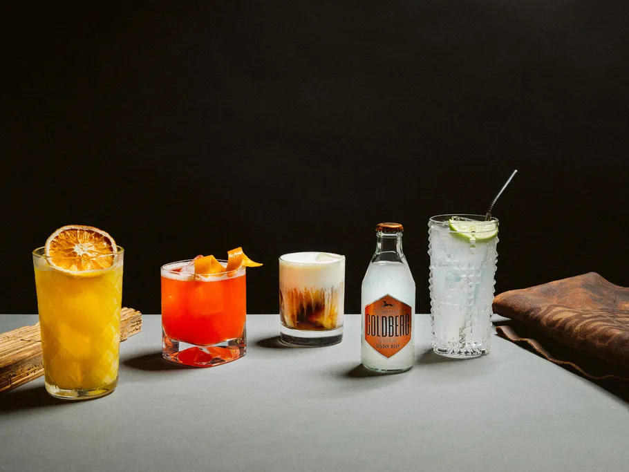 Fünf bunte Cocktails auf einem Tisch, dunkler Hintergrund.