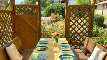 Holztisch mit gedeckten Tellern im Garten bei Sonnenlicht.