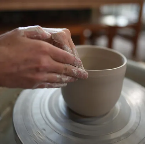 Töpfer formt einen schlichten, grauen Tonbehälter auf Drehscheibe.