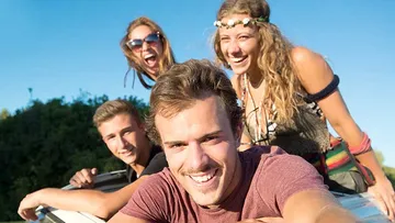 Vier junge Leute lachen auf einem Auto. sonniger Hintergrund.