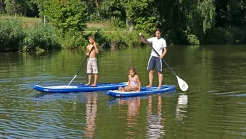 Three people stand in the water on stand-up paddle boards.
