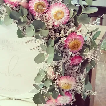 Blumenarrangement schmückt ein Willkommensschild zur Taufe.