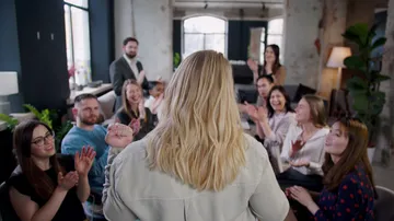 A person speaks, audience applauds in a modern setting.