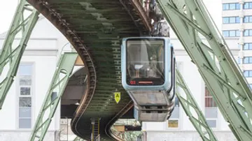 Seilbahn fährt über geschwungene Gleise in städtischer Umgebung.
