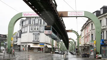 Schwebebahn fährt über eine nasse Straße in Wuppertal.