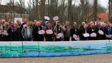 Menschen stehen mit Schildern vor einem gemalten Landschaftsbild.