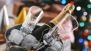 Champagne bottle and glasses rest in ice pools, festively decorated.