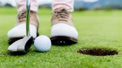 Golfspieler zielt mit Schläger auf Golfball nahe Loch.