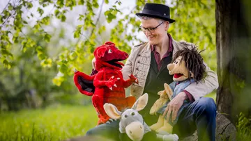 Puppenspieler sitzt mit Handpuppen in der Natur.