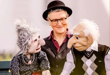 Puppenspieler interagiert mit zwei Puppen im Freien.