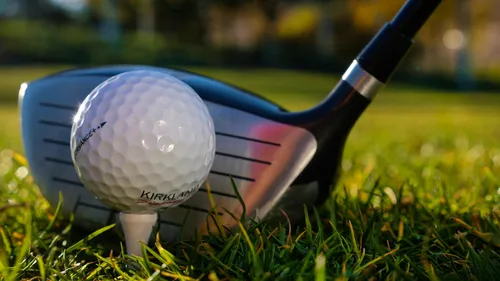 Golfball auf Tee neben einem Golfschläger auf Gras.