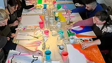 Teilnehmer malen zusammen an einem langen Tisch mit Farben.