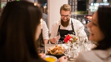 A man with a beard smiles and serves drinks at the table.