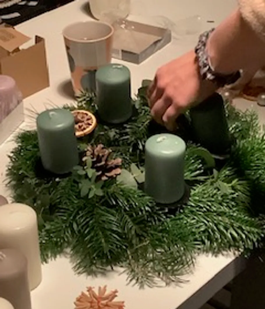 Hand arranging candles on evergreen wreath.