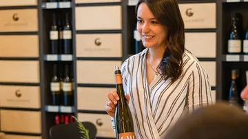 Woman holds wine bottle in wine shop and smiles friendly.