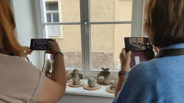 Zwei Personen fotografieren Skulpturen am Fenster.