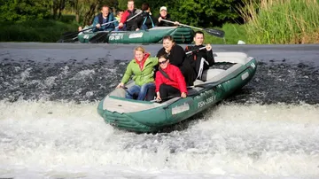 Lifeboat sails over waterfall surrounded by green nature.