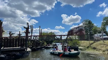 Canoeists paddle under a bridge on a wooded shore.