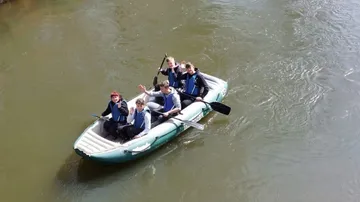 Five people are paddling in a boat on a river.