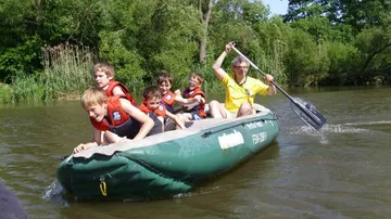 A group of children paddles in the water on a boat.