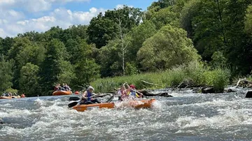 Kayaks travel through crashing water surrounded by trees.