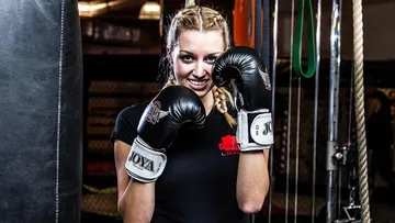 Female boxer with gloves smiles in a boxing studio.