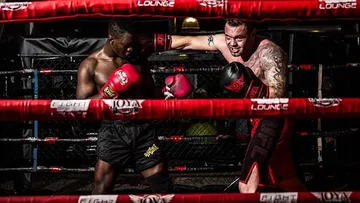 Two boxers fight in the ring with red rings.