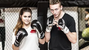 Two boxers pose in a training room wearing gloves.