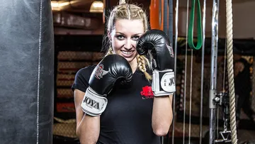 Junge Frau mit Boxhandschuhen lächelt in Fitnessstudio.