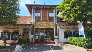 Restaurantfassade mit großem Fenster, umgeben von Bäumen.