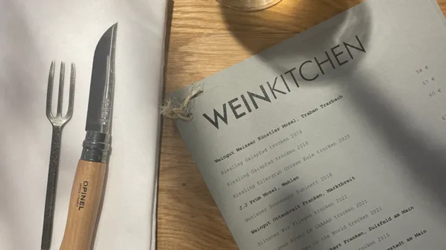 The fork and knife are on the table next to a wine list.