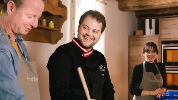 Chefs smile and cook in a cozy kitchen scene.