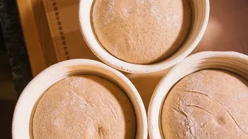 Three round dough bowls rest on a wooden surface.