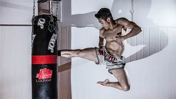 Ein Kämpfer tritt gegen einen Boxsack in einem Trainingsraum.