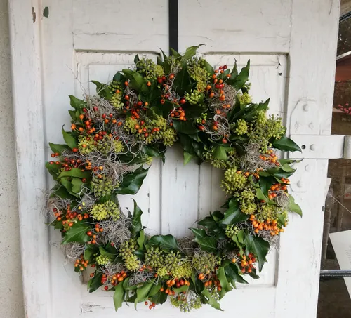 A wreath hangs on a white door, decorated with leaves.