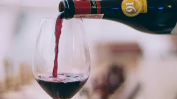 Rotwein wird aus einer Flasche in ein Glas gegossen.