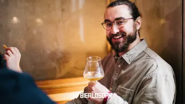 Mann mit Bierglas lächelt, entspannt in Bar-Umgebung.