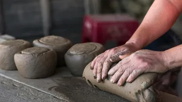 Hands knead clay on a table in a workshop.