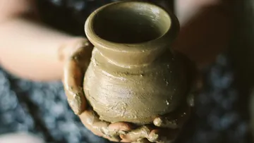 Clay pot is held in hands by a person.