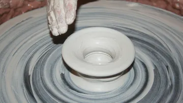 Rotating pottery wheel shapes wet clay pot in workshop