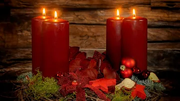Three red candles burn on a decorated Christmas wreath.