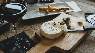 Rotwein und Käse auf einem Holzbrett, Snacks im Hintergrund.