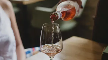 Eine Flasche schenkt Roséwein in ein Glas.
